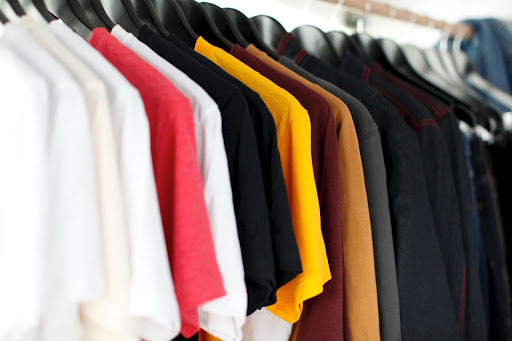 White, red, black, golden yellow and gray t-shirts on hangers hanging on a clothes rack. 