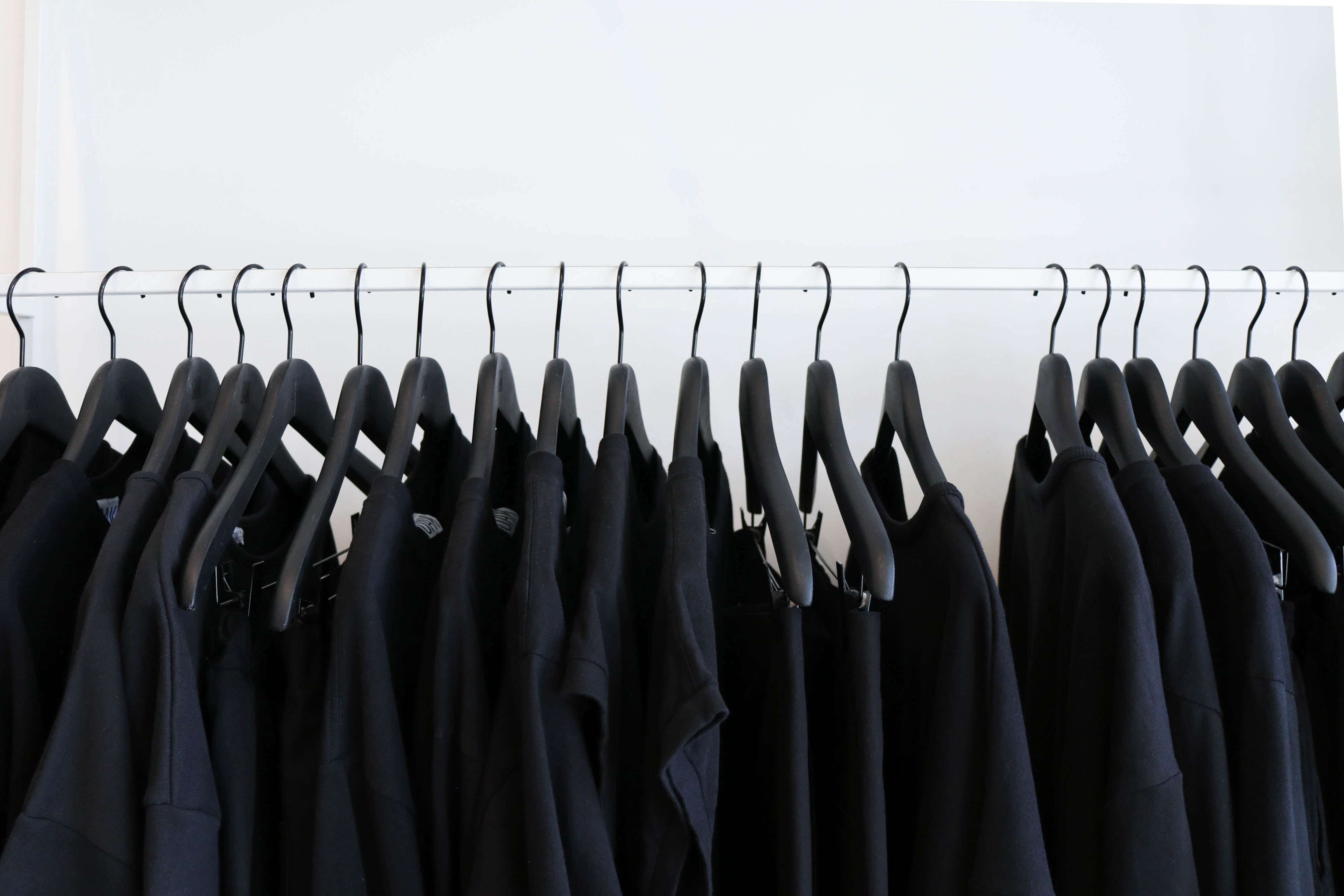 Black t-shirts on hangers hanging from a clothing rack.