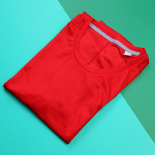 Bright red blank shirt folded nicely on a green background.