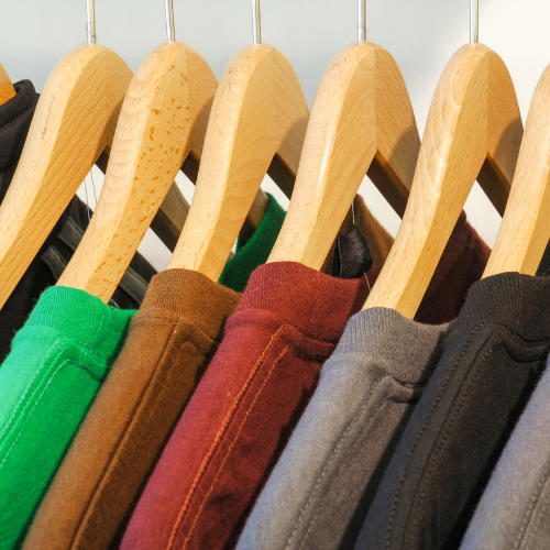 Different colored t-shirts hanging on hangers in this order from left to right: green, camel, red, gray, black and gray.
