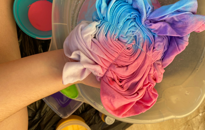 Person holding a pink purple and blue spiral tie dyed shirt in a bowl that is folded and tied 