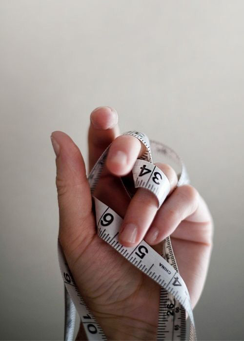 Person holding a fabric measuring tape, woven between their fingers. 