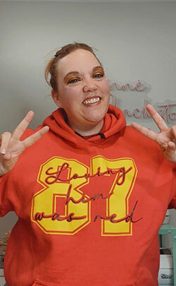 Corinne Blackstone modeling a red hoodie from ShirtSpace, printed with the Taylor Swift song lyrics “loving him is red” and Travis Kelce’s Kansas City Chiefs team number, 87.