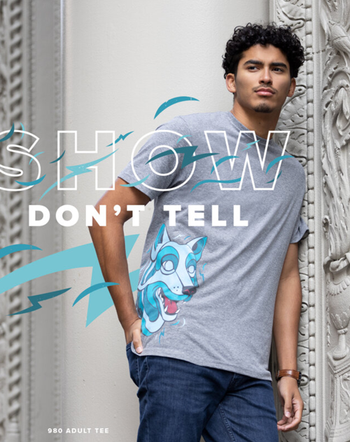 Man wearing a gray Anvil by Gildan 980 t-shirt that has a blue wolf printed on the side. The text reads “Show Don’t Tell”.