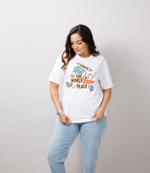 Woman wearing white t-shirt with the words “bake the world a better place” and baking tools
