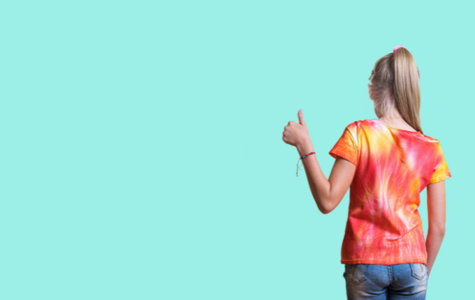 Young girl wearing a tie dye shirt with her back to us giving a thumbs up with her hands