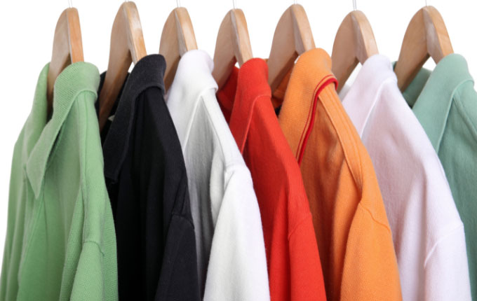 Light green, black, orange, red and white pique polo shirts hanging on a rack. 