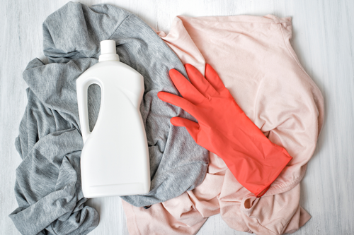 Heather gray and light pink t-shirts messily laying flat with a white jug of bleach and red rubber gloves resting on top. 