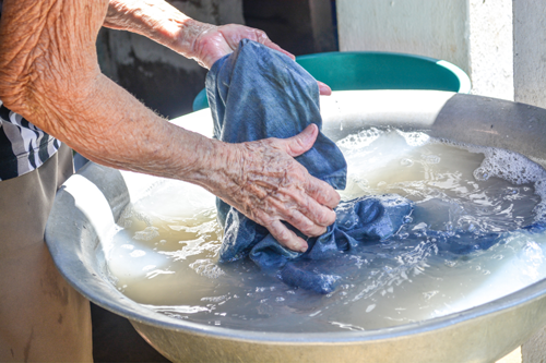 Elderly man's arms washing a t-shirt in large basin of water to fade it. 