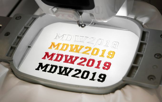 Digitized embroidered design reading MDW 2019 in white, yellow, red and black thread. 