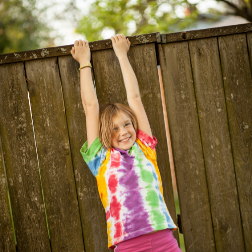 Kid hanging from a fence, happy and wearing a tie-dye shirt.