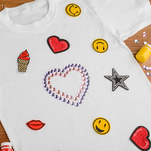 A plain white t-shirt decorating with different heart and smiley face iron on patches.