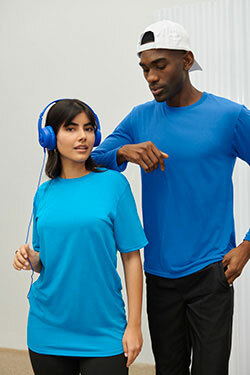 A woman wearing listening to music through blue headphones while wearing the Gildan G420 Performance® T-Shirt in sapphire and a man with her that is resting his arm on her should while wearing the Gildan G424 Performance® Long Sleeve T-Shirt in royal and a backwards white snapback cap, all available to buy from ShirtSpace. 