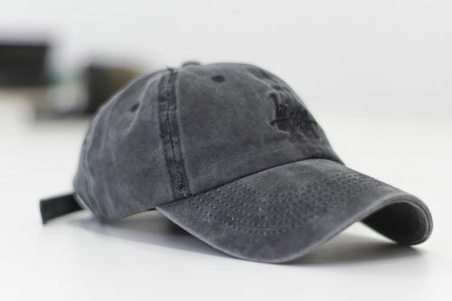 A garment-dyed, unstructured charcoal baseball cap with hook and loop closure and a black embroidered design on the front. 