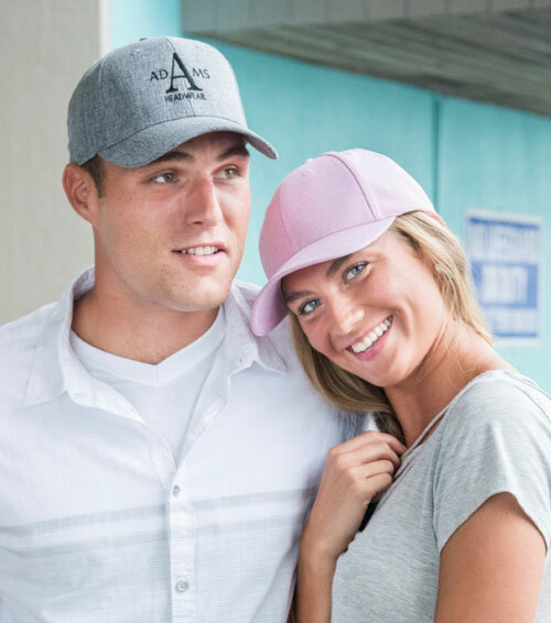 A man and women wearing the Adams DX101 Deluxe Cap in charcoal and pale pink, both available wholesale-priced from ShirtSpace, and ready for embroidery. 