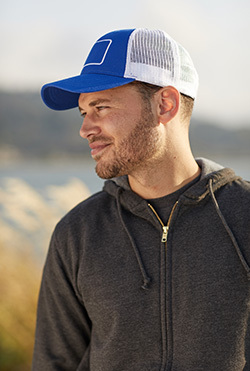 A man wearing a charcoal gray full-zip sweatshirt and a Big Accessories BA656T Patch Trucker Cap in royal/white/white, available from ShirtSpace. 