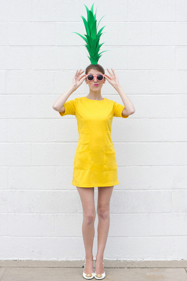 A woman wearing a yellow t-shirt dress and green leaf headband to create a pineapple costume. 