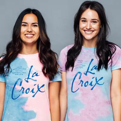 Two women wearing pink, blue and purple tie-dyed t-shirts that have been printed with the La Croix logo. 