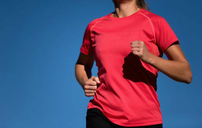 A woman wearing a red polyester athletic t-shirt while jogging.