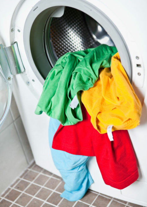 A dryer with bright, colorful t-shirts spilling out. 