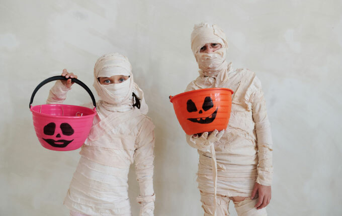 Two children dressed as mummies for Halloween with their trick-or-treat pails. 