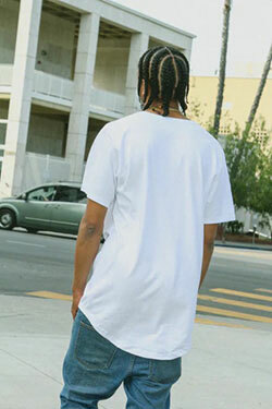 Back view of a man in an urban setting, wearing jeans, street sneakers and an oversized white tee from Shaka Wear.