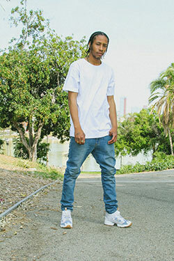 Man in an urban setting, wearing jeans, street sneakers and an oversized white tee from Shaka Wear.