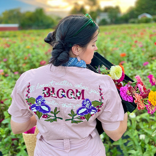 Woman in field of flowers wearing a pink embroidered shirt