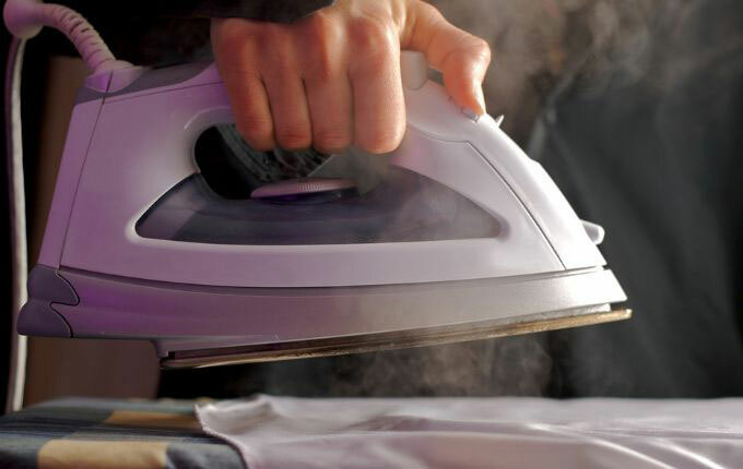 A steaming hand held iron used to get wrinkles out of clothes, such as t-shirts.