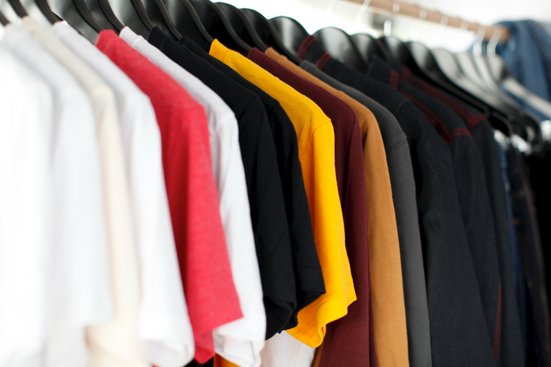 White, red, black, gold, maroon and tan t-shirts from ShirtSpace hanging on a clothes rack.
