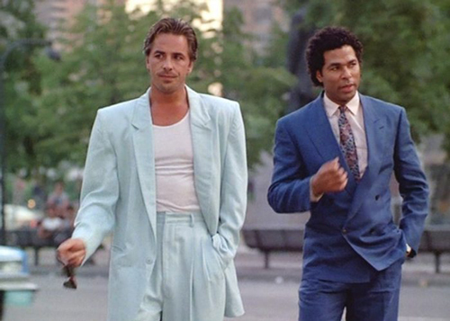 Actors Don Johnson and Philip Michael Thomas, starring in 1980’s popular TV show, Miami Vice. Don Johnson wears a white t-shirt under a light blue suit with shoulder pads.