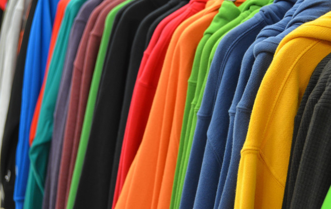 Multi-colored hooded sweatshirts hanging on a clothes rack.
