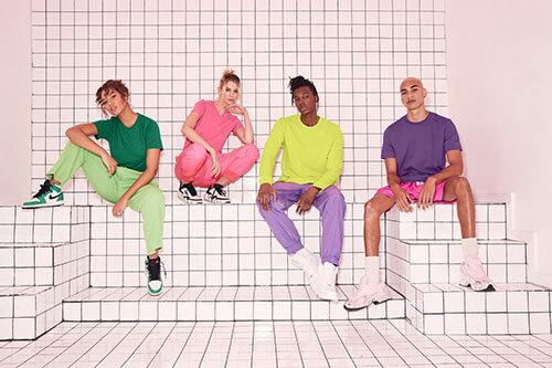 People sitting against a white tiled background while wearing Bella+Canvas t-shirts in bright colors and color-blocked outfits. 