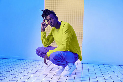 Man wearing the Bella+Canvas 3501 long-sleeved t-shirt in the neon yellow color “strobe”, paired with “royal purple” pants. 