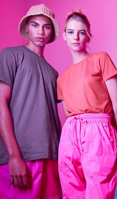  A man and woman wearing Bella+Canvas t-shirts in the colors “dark lavender” and “neon pink”, paired with bright pink pants,