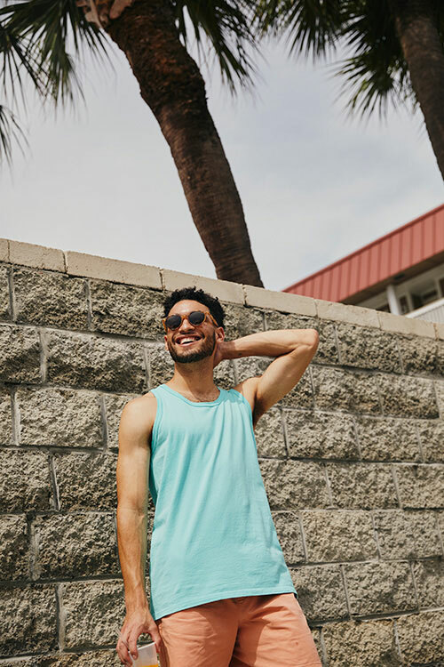 Man wearing a light blue GDH300 tank top from ComfortWash by Hanes, paired with peach-colored shorts. 