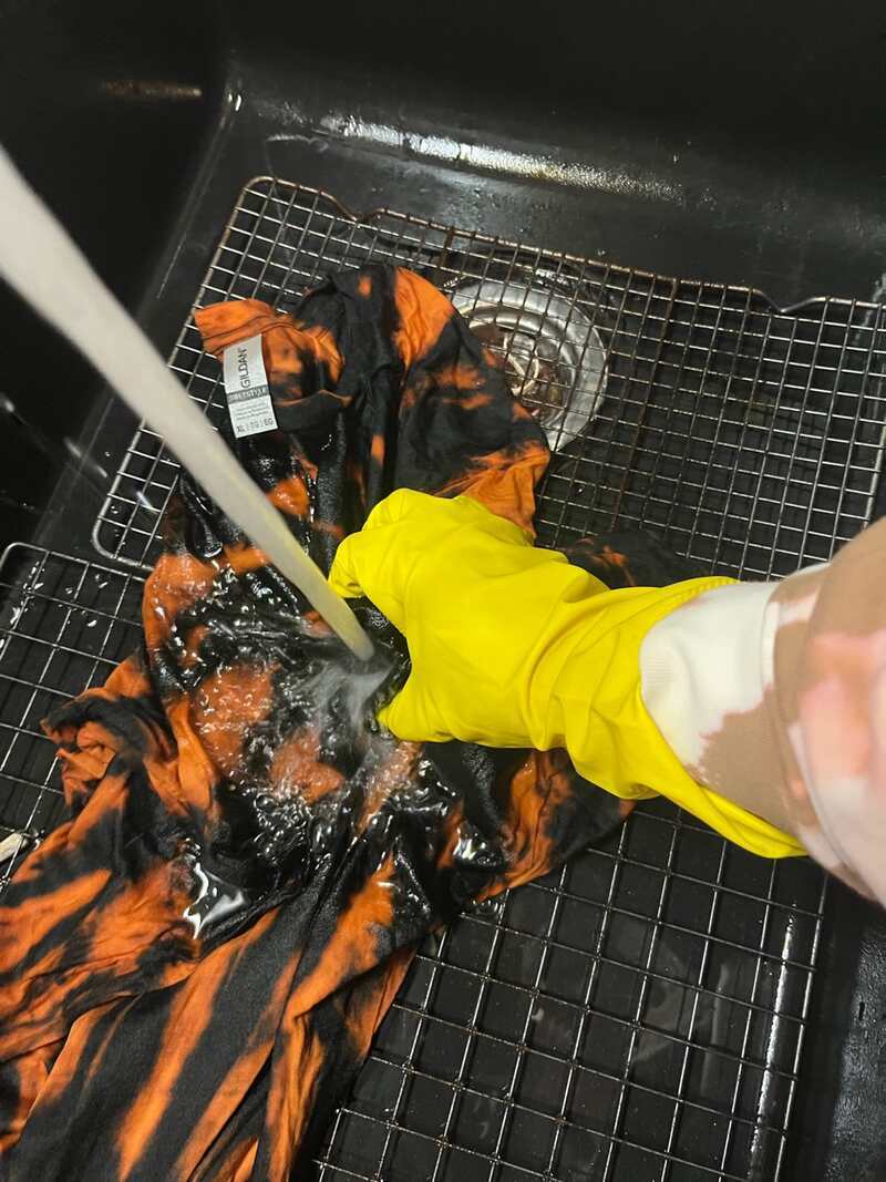 Rinsing a freshly bleached Gildan t-shirt with cold water while wearing yellow rubber gloves.