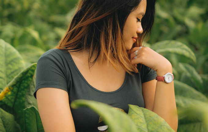 Woman wearing a scoop neck t-shirt in front of green foliage.