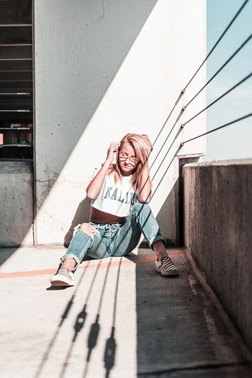 A woman sitting on the ground in a parking garage, wearing ripped jeans and a DIY cropped t-shirt. 