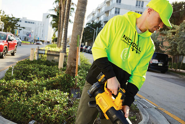 Man wearing a Cornerstone black and safety yellow color-blocked pullover hoodie while landscaping.