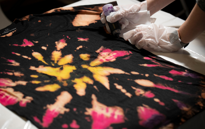 Gloved hands applying purple dye to bleached area of a reverse tie-dyed black t-shirt.