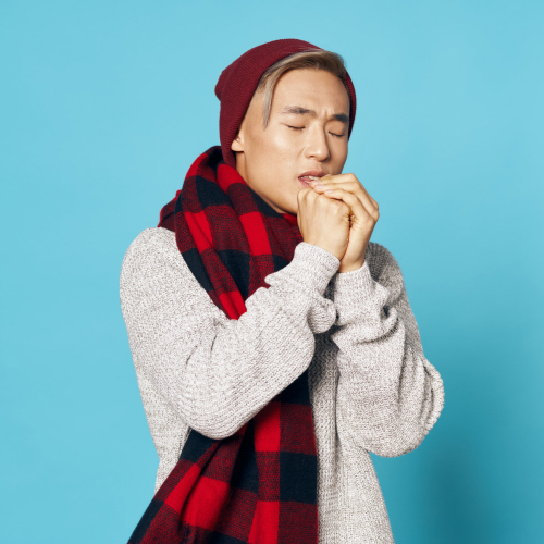 Cold man wearing red and black checkered buffalo plaid scarf, gray sweater and maroon beanie with an aqua blue background.