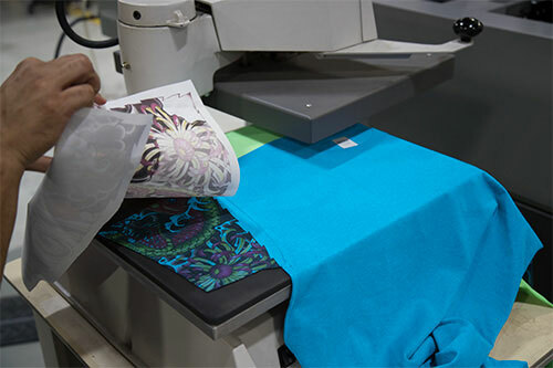 Blue Gildan t-shirt sitting on a heat press with sublimation sleeve prints being applied.