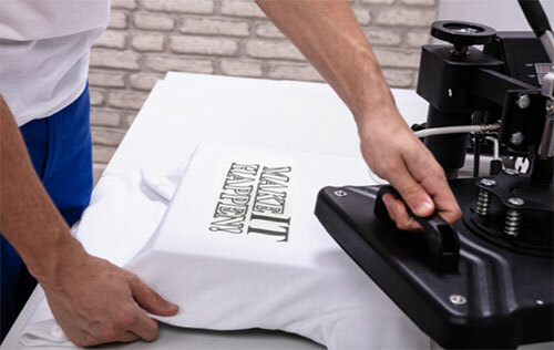 Person heat pressing white t-shirt with a sublimation print that says “Make it Happen!” in black lettering.
