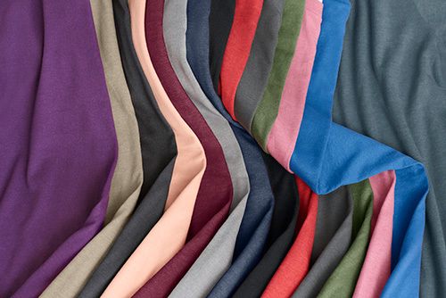 Many colors of the Gildan G670 Men's Softstyle CVC T-Shirt laid out flat and attractively displayed in a partially folded manner. 