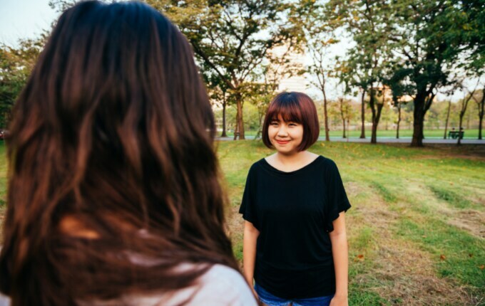 Two women facing each other. The one who's face is visible is wearing a black boat neck t-shirt. 