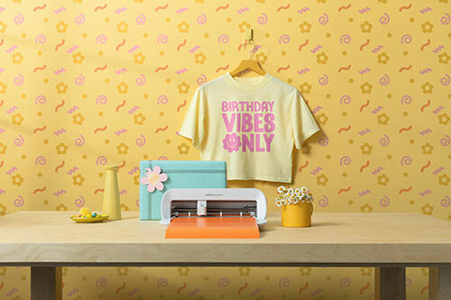 A yellow crop top t-shirt with pink text printed on it that reads, “Birthday Vibes Only”, displayed with a Cricut Joy vinyl cutter. 
