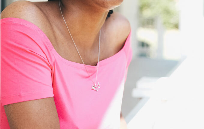 Woman wearing a pink off-the-shoulder top and silver necklace on a chain.