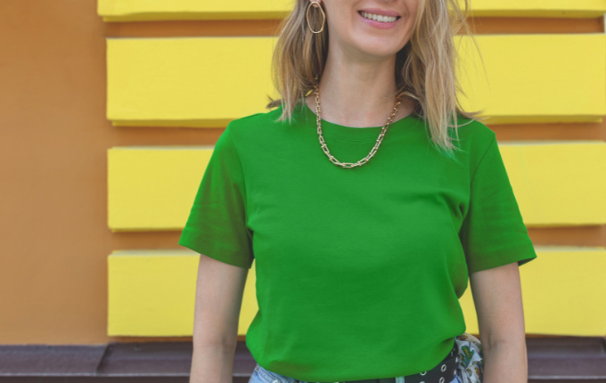 Woman wearing a green crewneck t-shirt with gold earrings and a chain necklace.