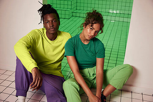 A man and woman wearing color-blocked outfits, which include Bella+Canvas 3501 in “Strobe” and 3413 triblend in “Kelly Green”.